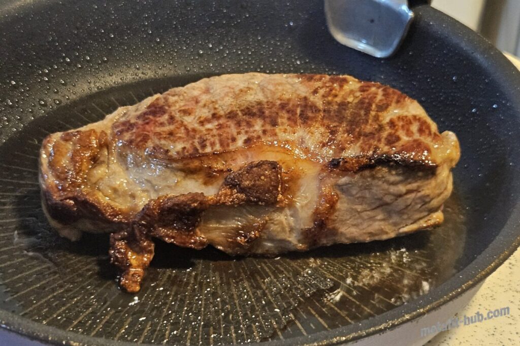 フライパンで焼いたステーキ肉の表面にこんがりと焼き色が付いた状態の画像